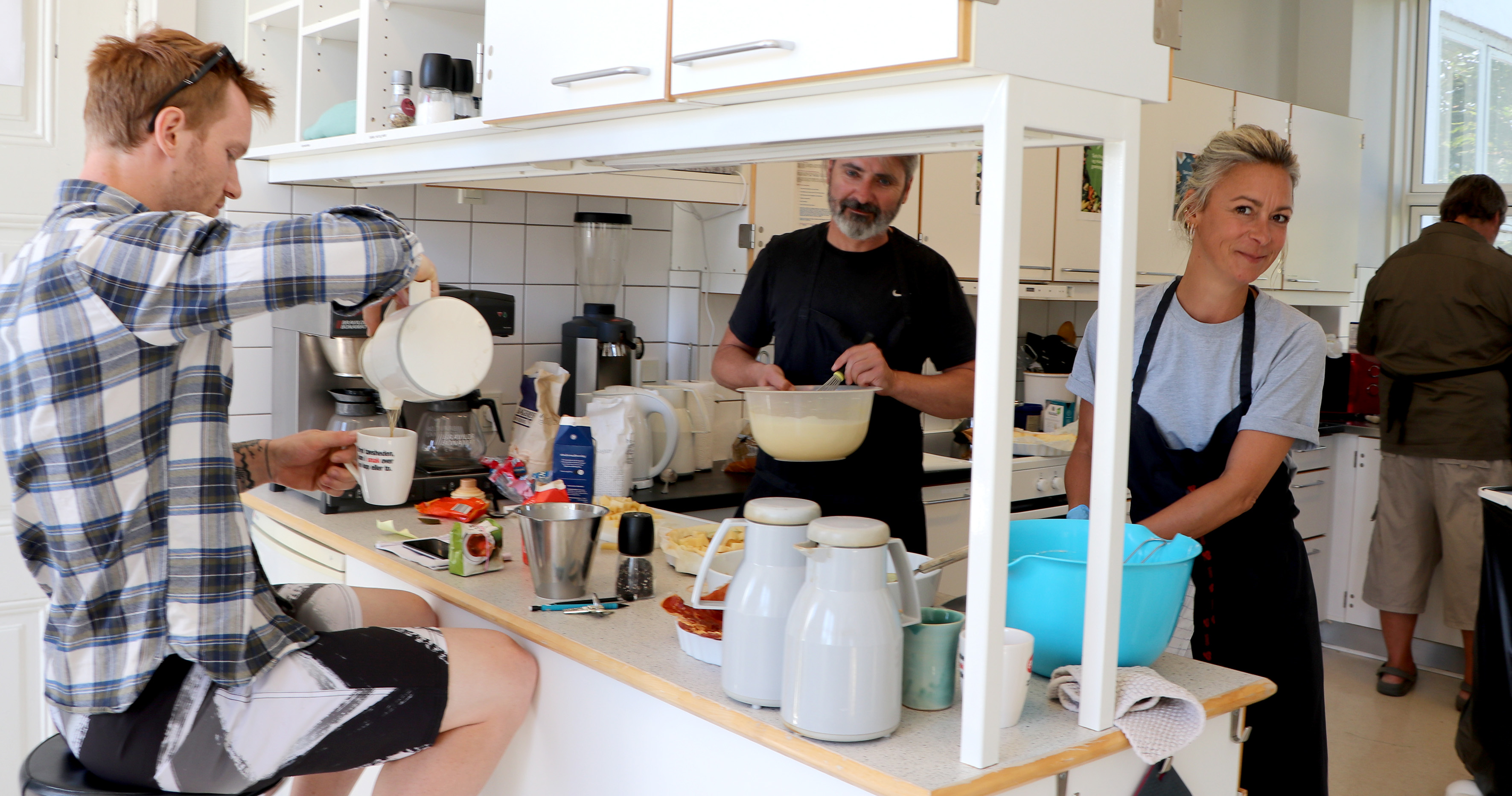 Billedet viser køkkenet i Sundhedscenter Hvide Hus, hvor Jacob Mols er ved at skænke kaffe, mens Signe Kromann Østergaard laver mad.