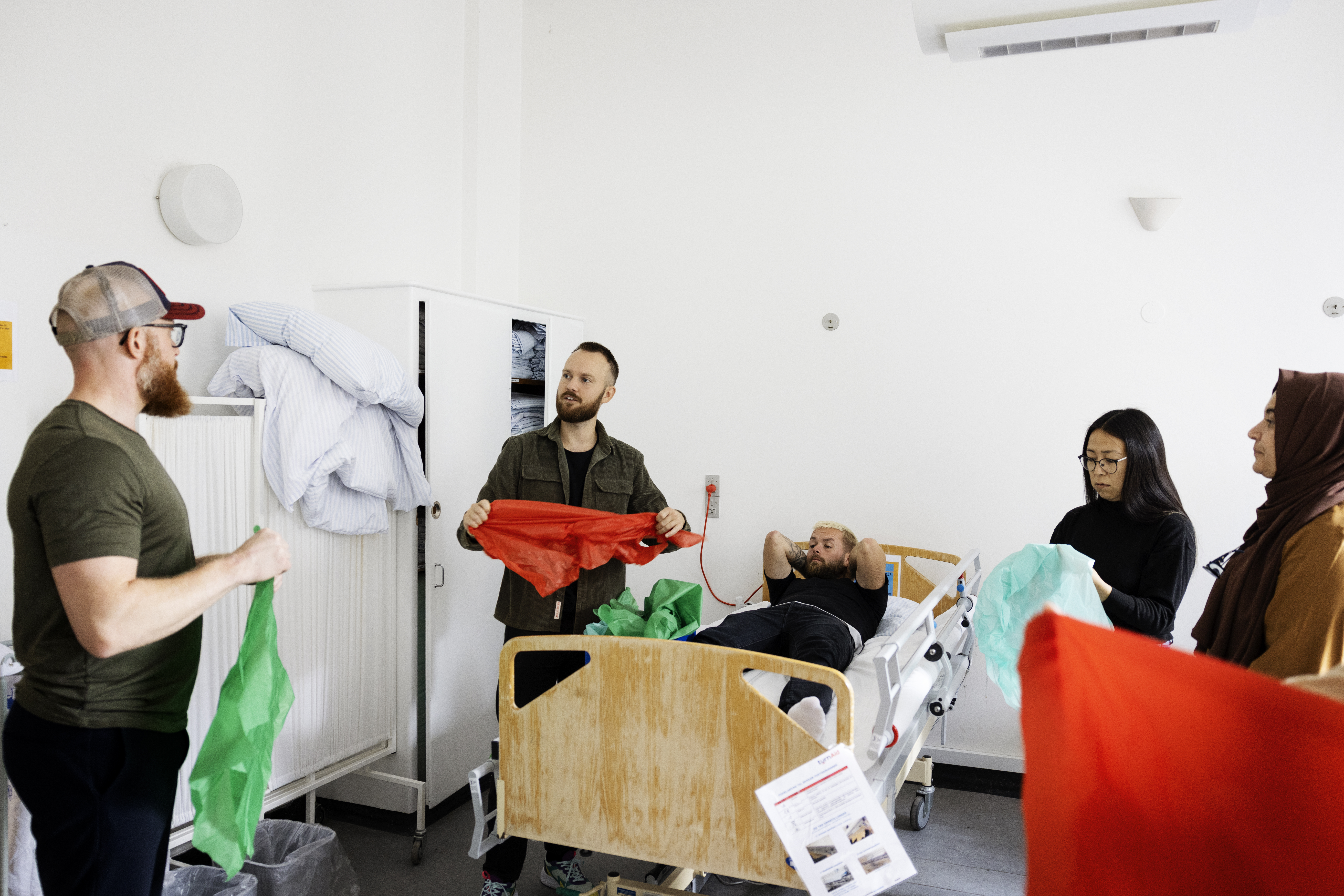 Billedet viser mennesker omkring en patientseng.