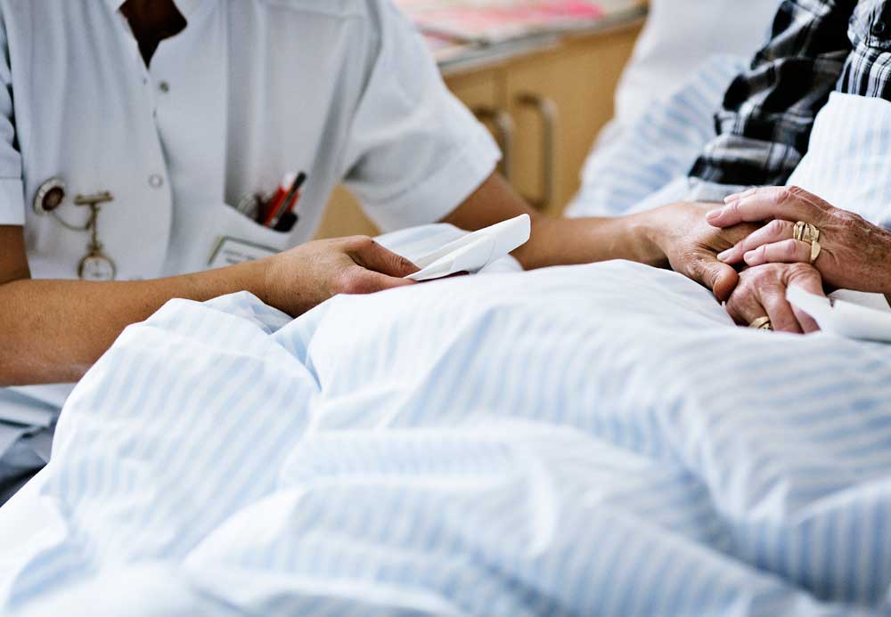 Billedet viser hænerne af en sygeplejerske, der holder en patient i hånden.