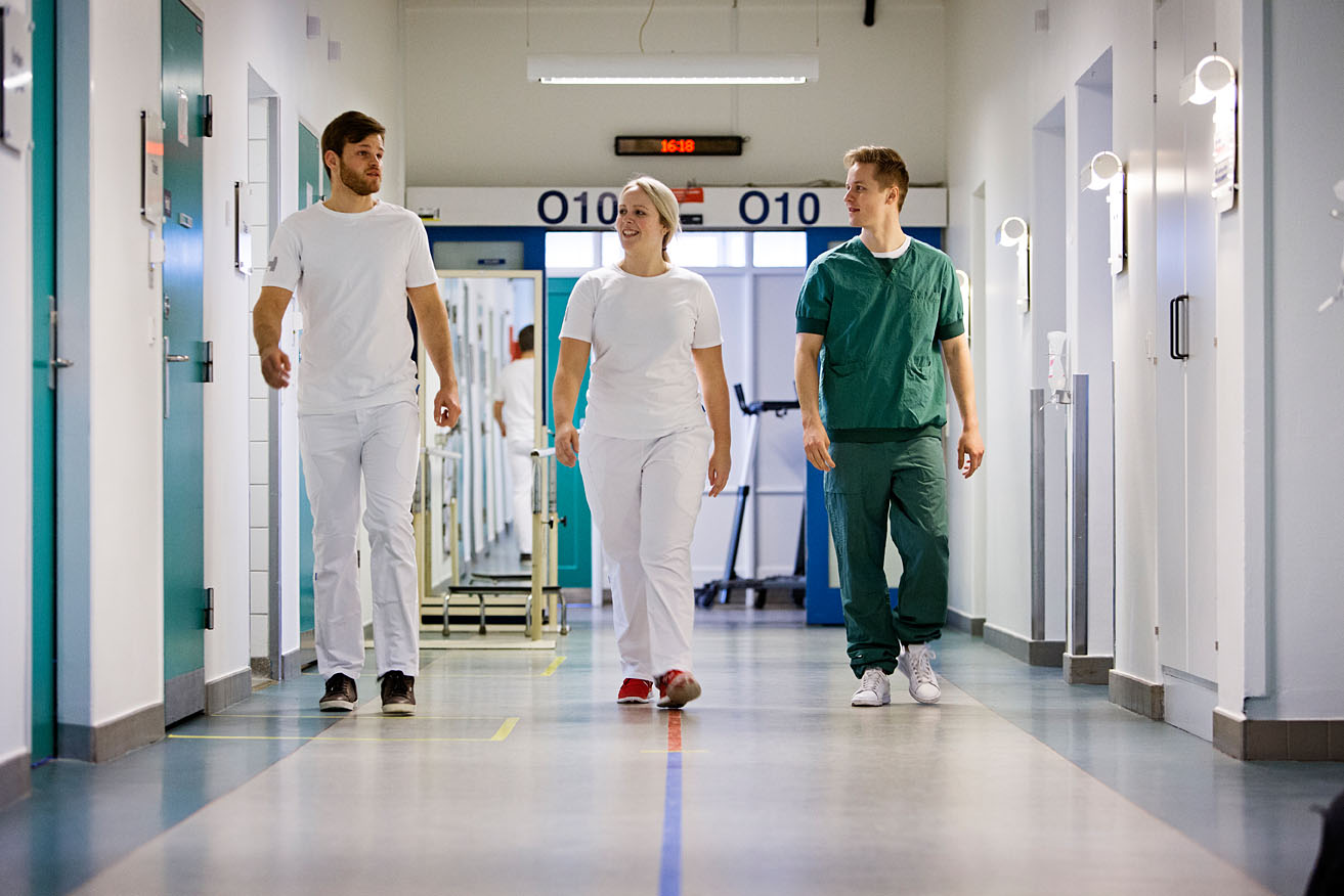 Billedet viser tre sygeplejestuderende, der går på en hospitalsgang.