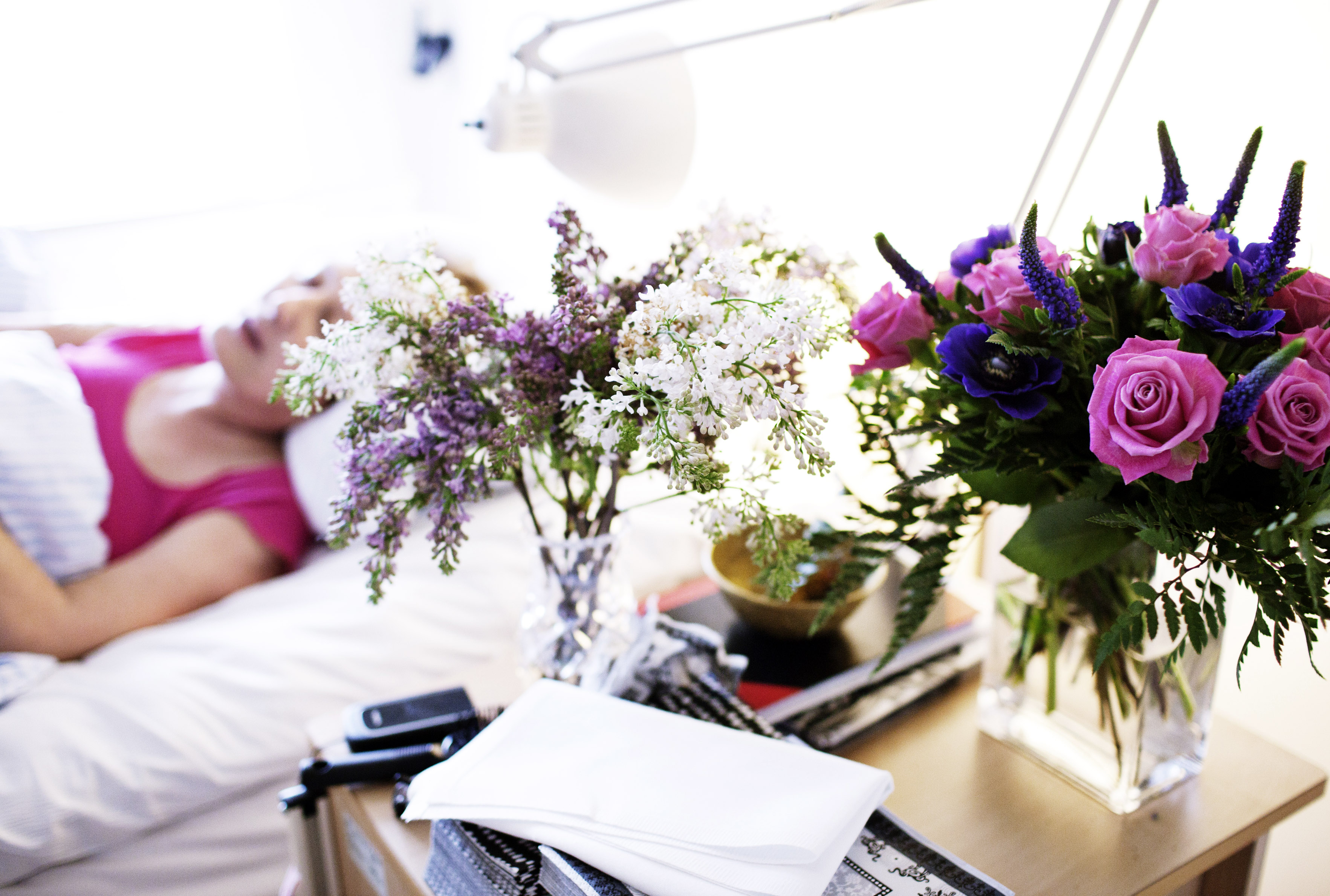 Billedet viser en patient i en seng og blomster i vaser i forgrunden.
