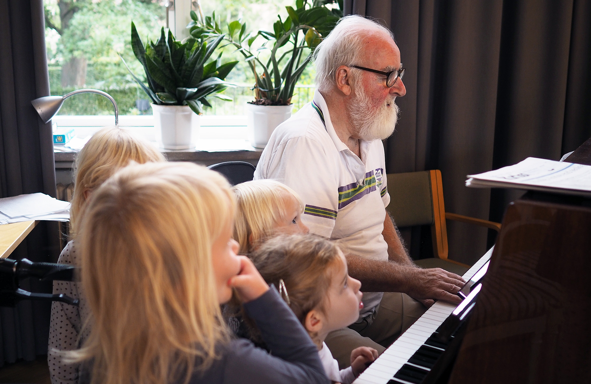 En beboer spiller klaver, mens fire børnehavebørn lytter interesseret.