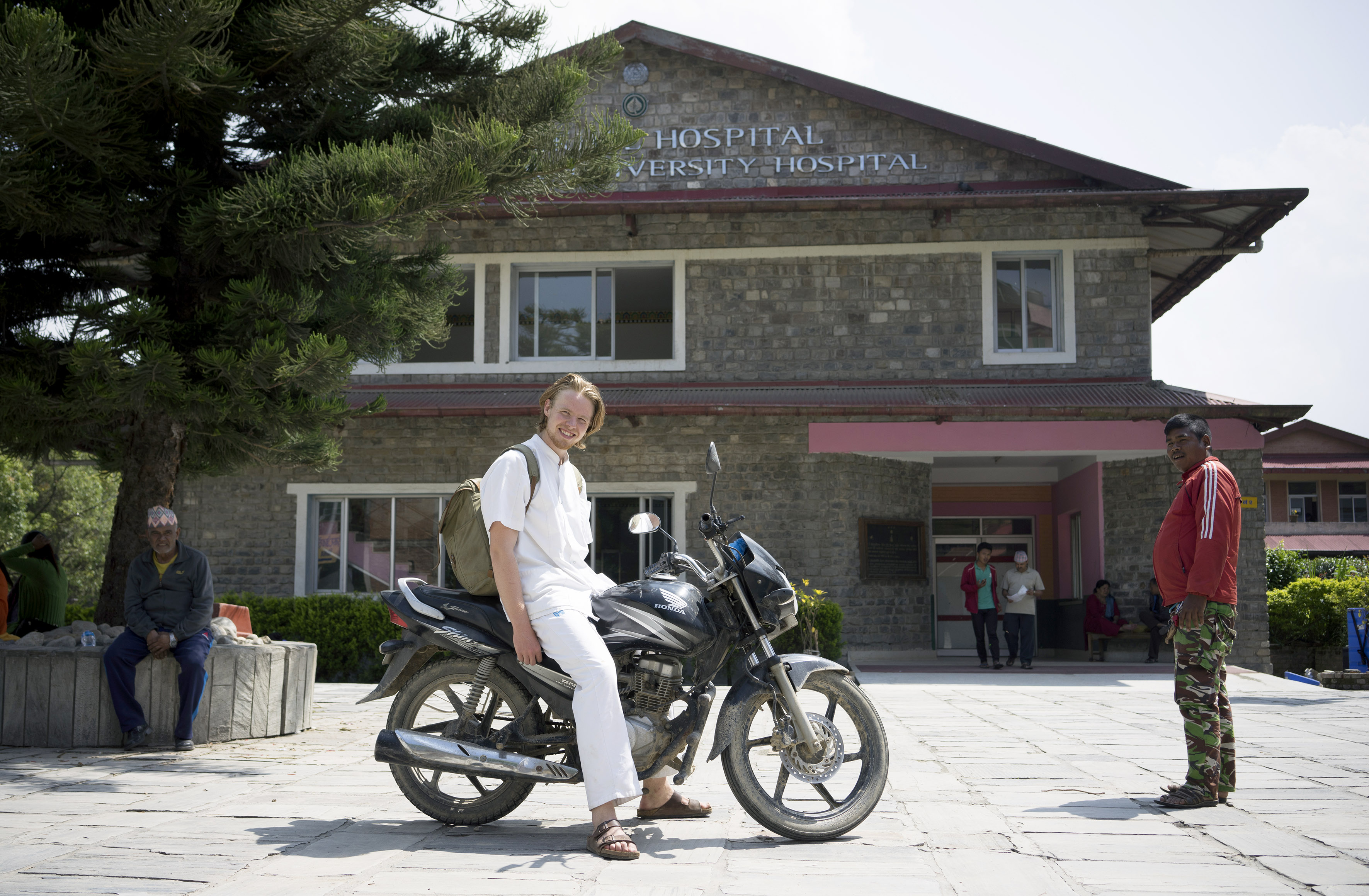 En ung mand på en motorcykel foran et hospital i Nepal.
