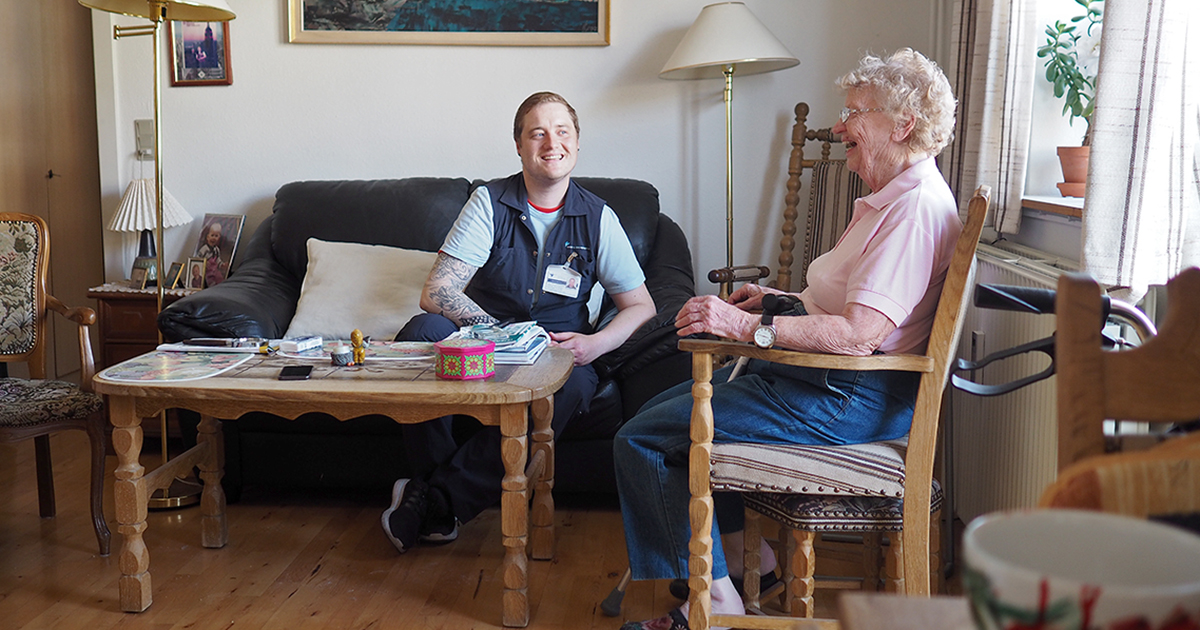 En ældre kvinde sidder og griner sammen med en medarbejder fra hjemmeplejen.