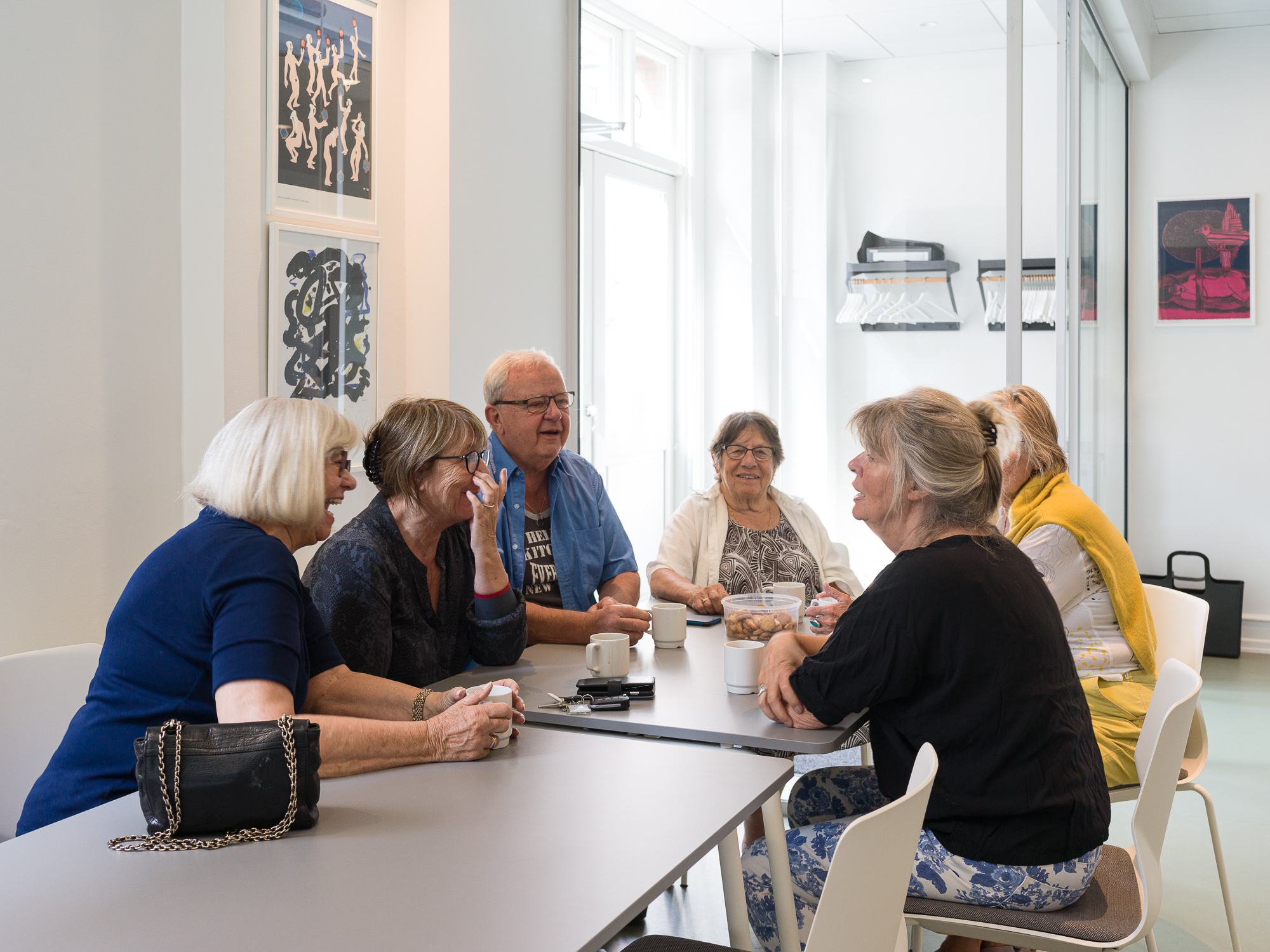 Billedet viser seks beboere, der taler sammen ved et bord i fælleslokalet. Foto: Hampus Berndtson.