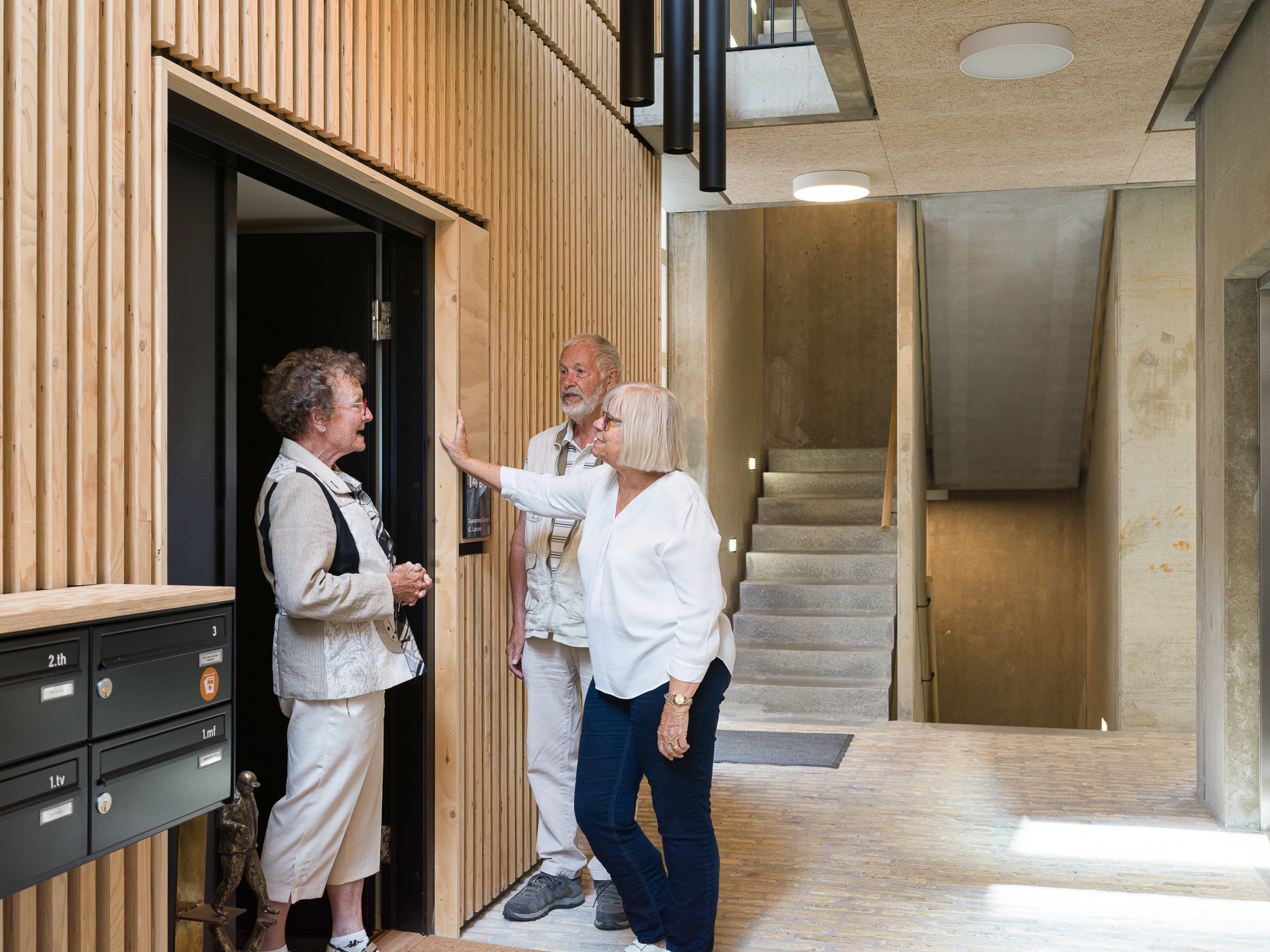 Billedet viser tre beboere i samtale ved en hoveddør i seniorboligerne. Foto: Hampus Berndtson.
