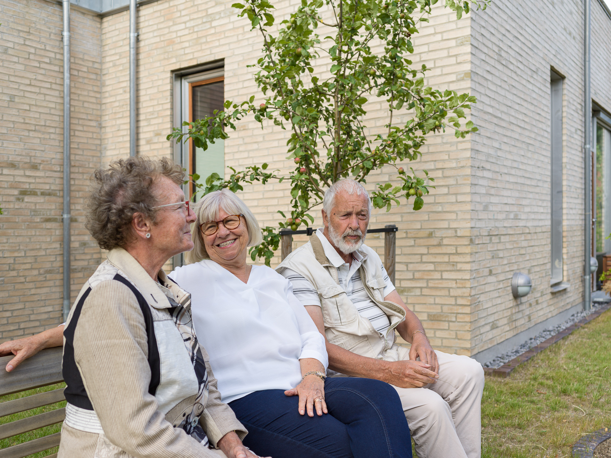 Tre beboere sidder på en bænk foran seniorboligerne. Foto: Hampus Berndtson.