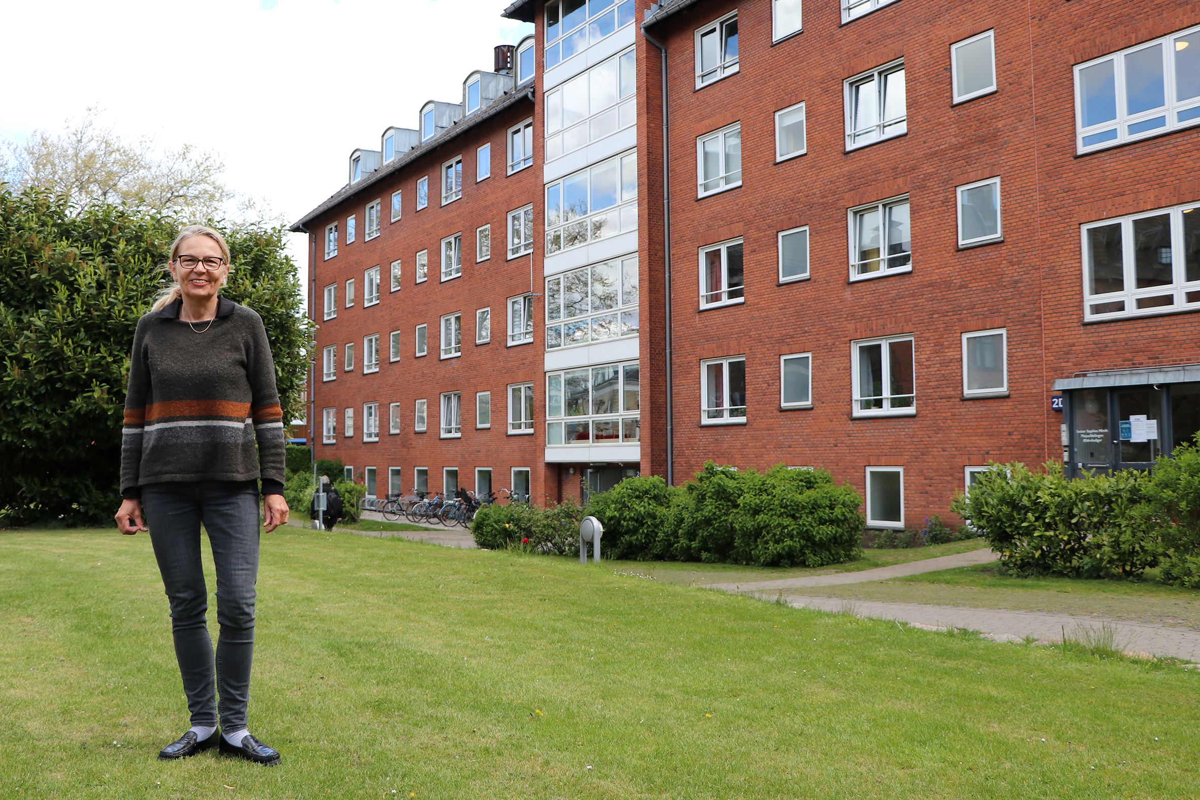 Hanne Munkholm står på en græsplæne foran en rød bygning, som rummer Søster Sophies Minde.