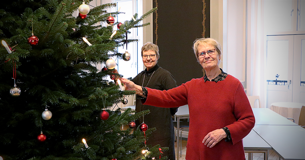 To kvinder er ved at pynte et stort juletræ.