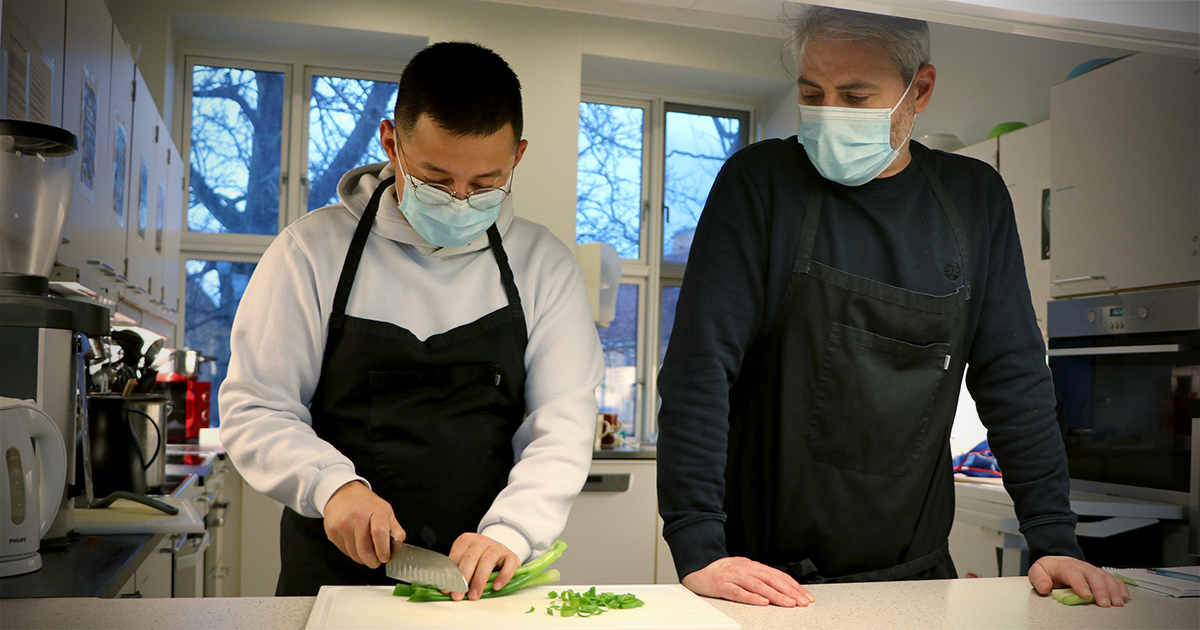 To personer iført mundbind snitter grøntsager i et køkken.