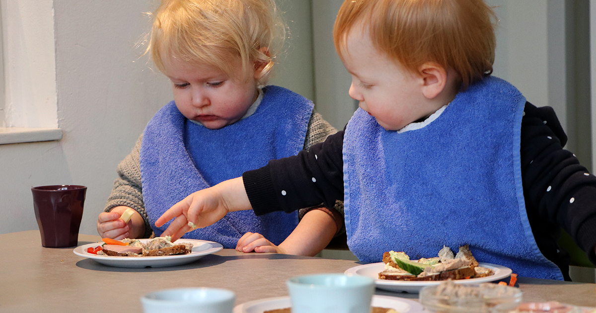 Foto af to børn som deler mad på en tallerken.