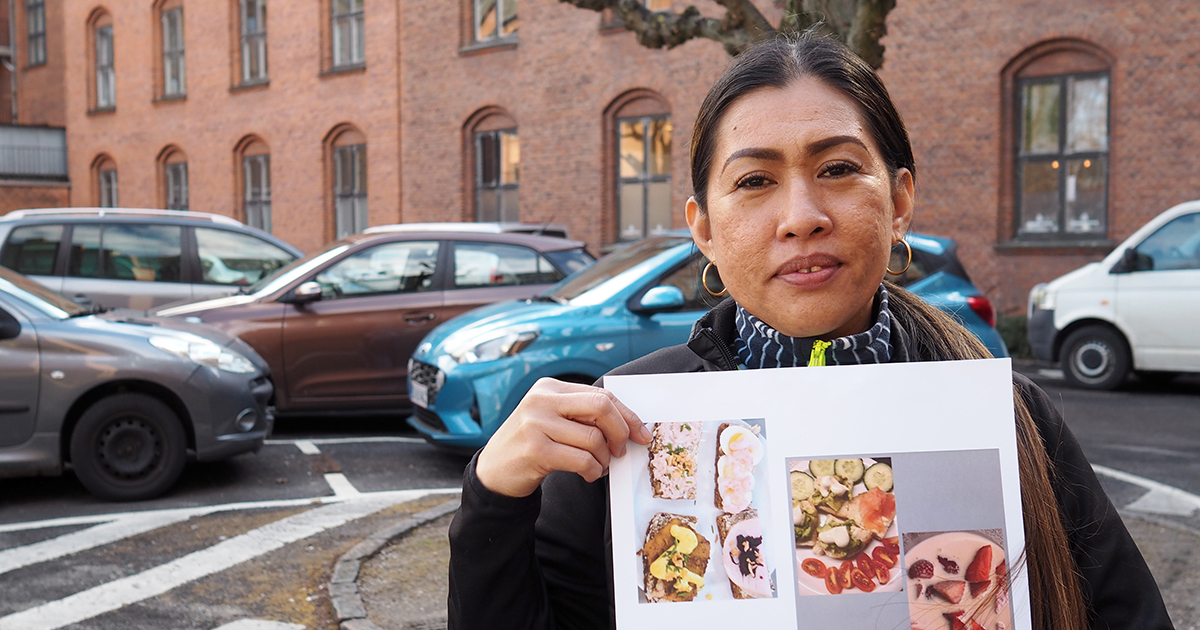 Coneluz Sonico Nørregaard foran Diakonissestiftelsens røde bygninger. Hun holder en plakat med mad i hænderne.