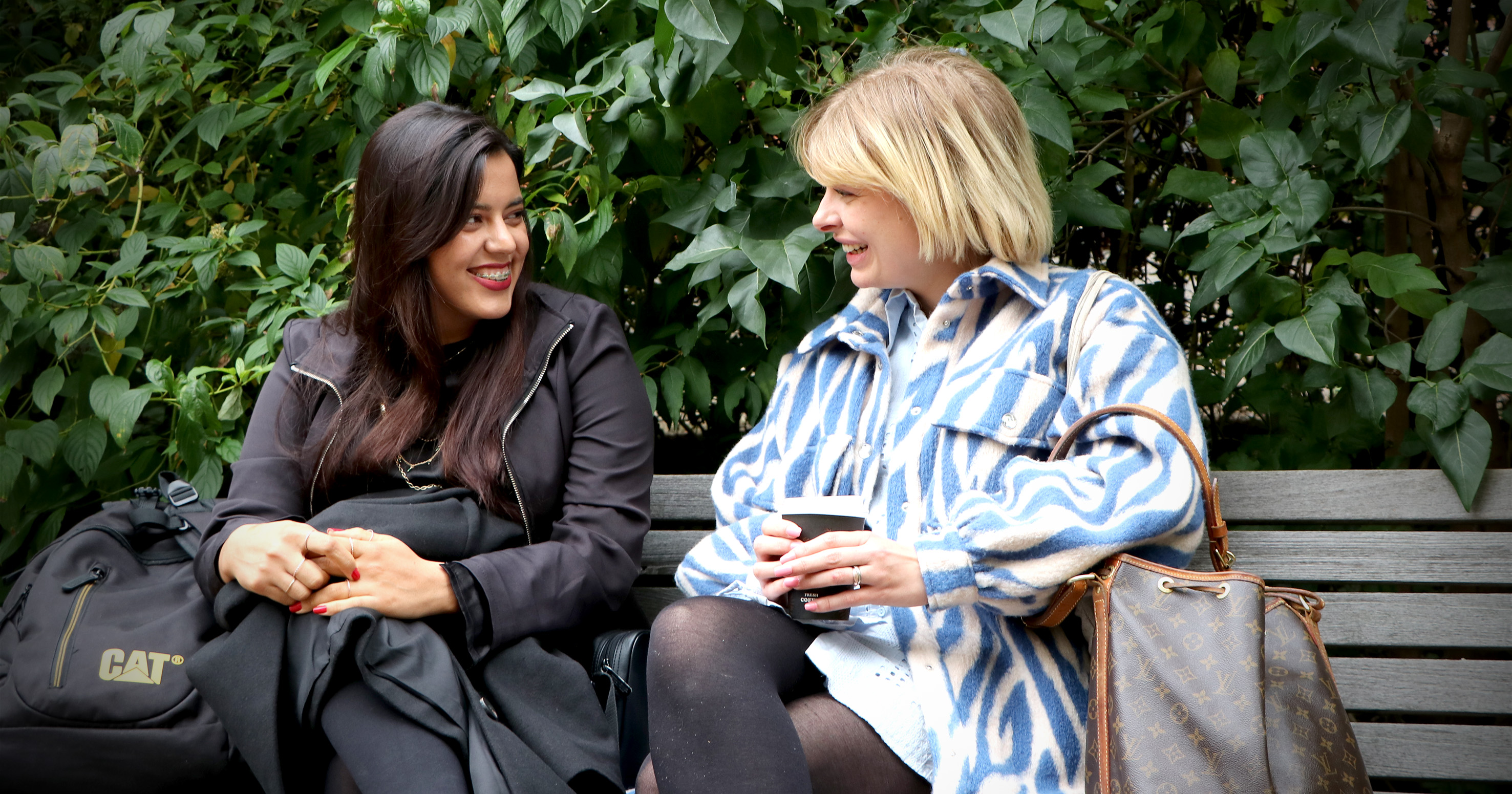 To kvinder sidder på en bænk og smiler til hinanden.