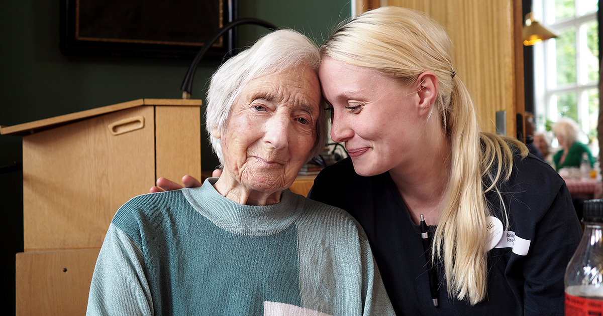 En ældre kvinde på plejehjem sidder tæt sammen med en medarbejder.
