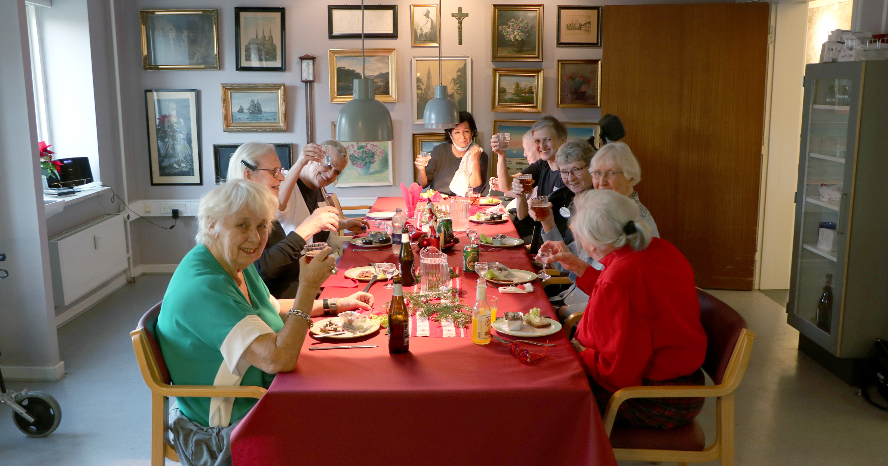 Billedet viser personer som spiser julefrokost rundt om en dækket bord.