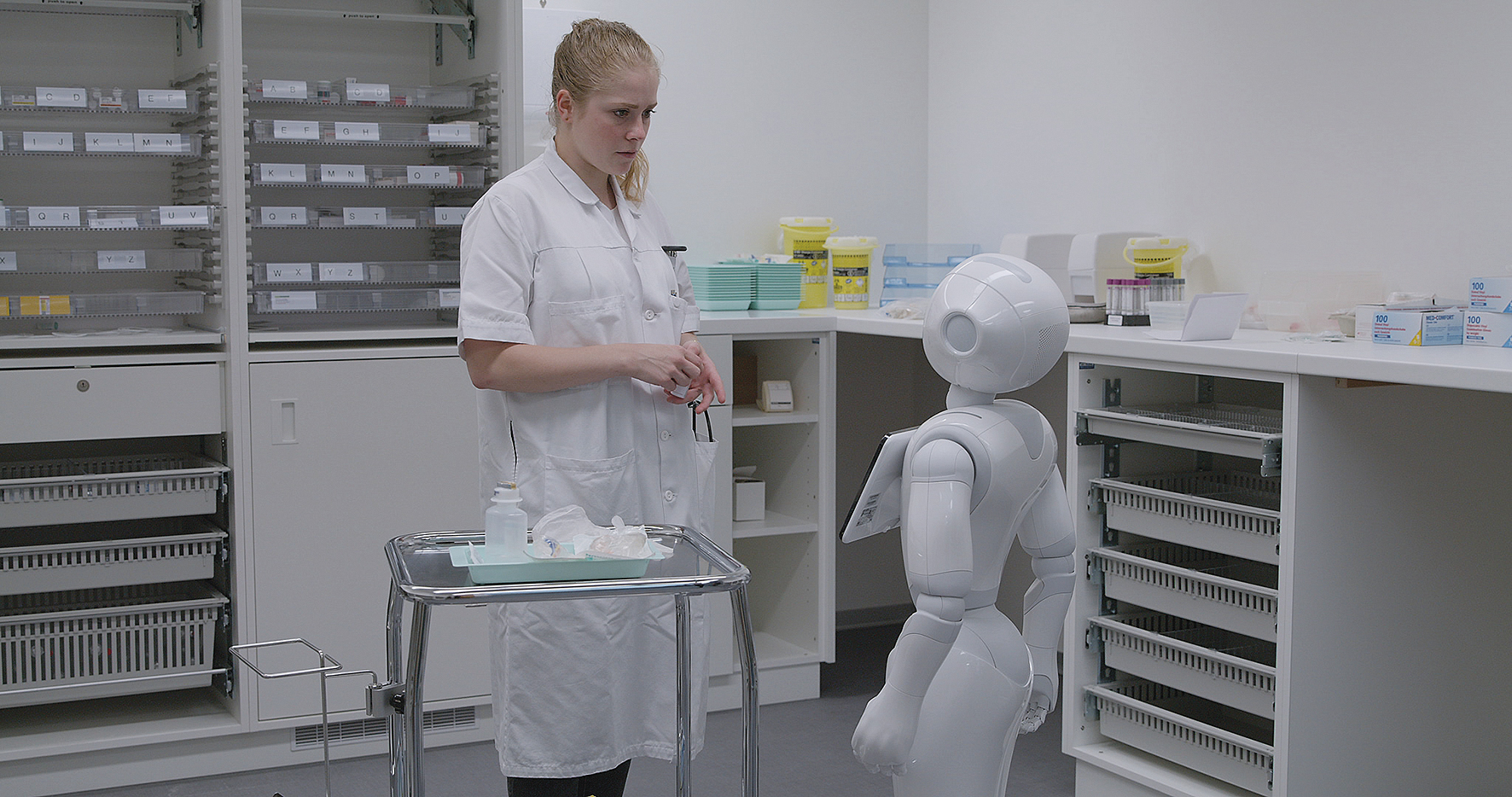 En kvinde i en hvid kittel ser på en robot.