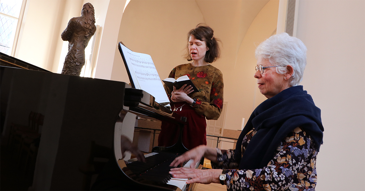 En kvinde synger og en anden spiller klaver.