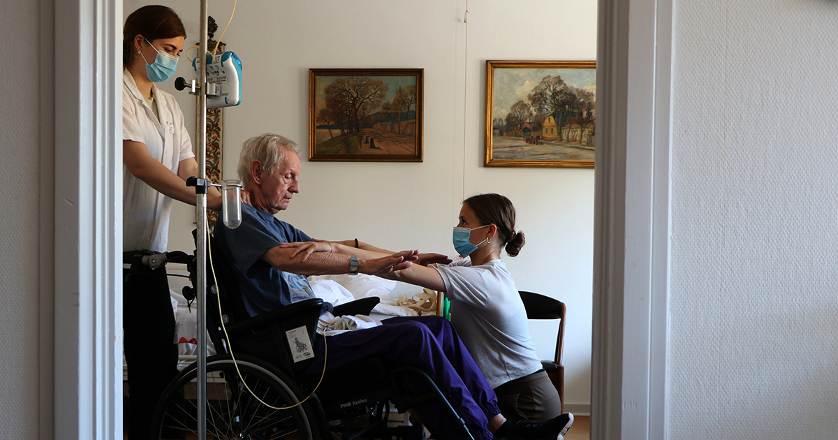 Billedet viser to kvinder som giver behandling til en ældre herre.
