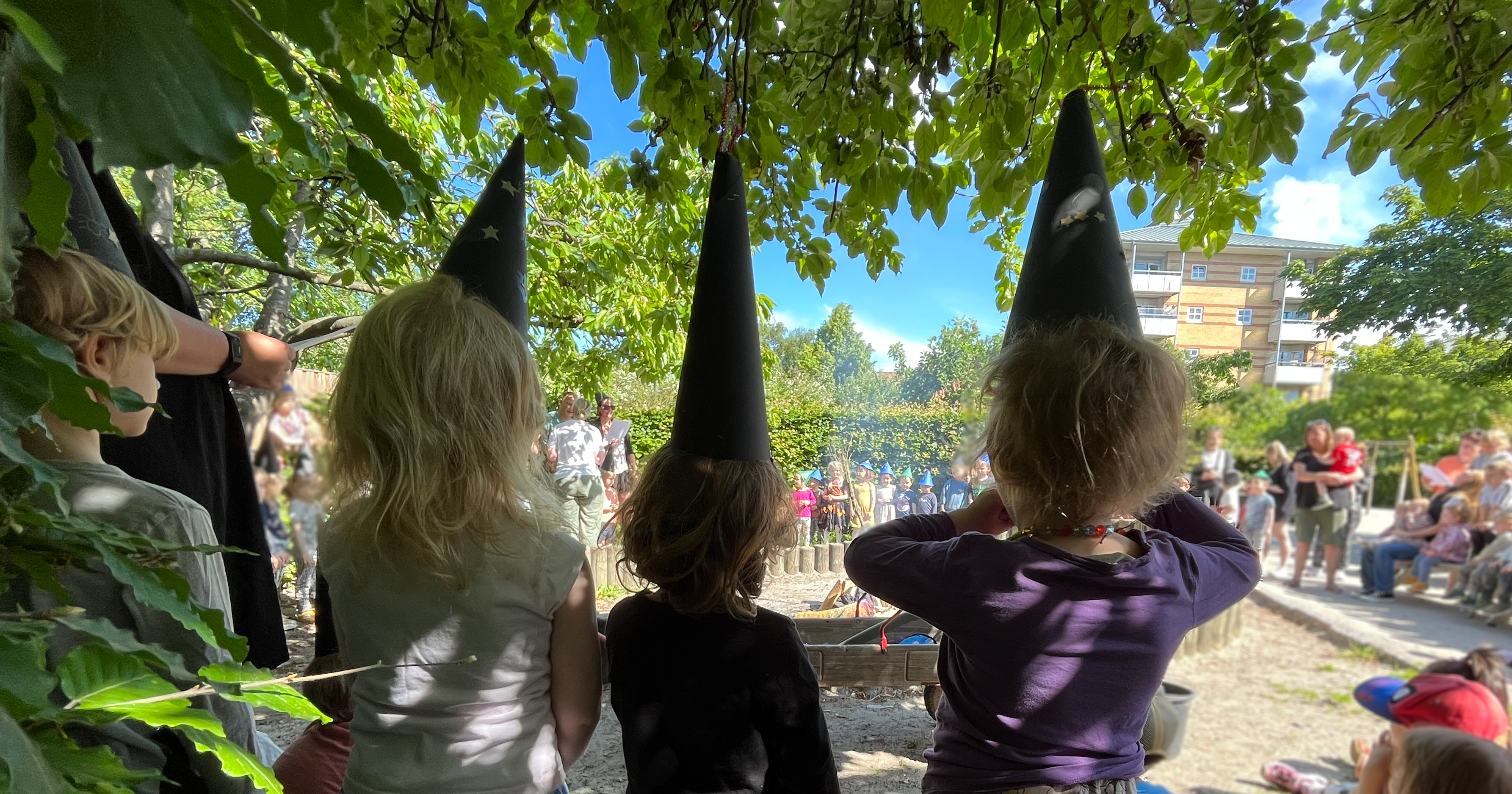 Billedet viser tre børn med spidse hatte i pap.