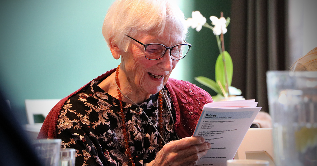 På billedet ser man en ældre kvinde som læser højt med et smil på læberne.