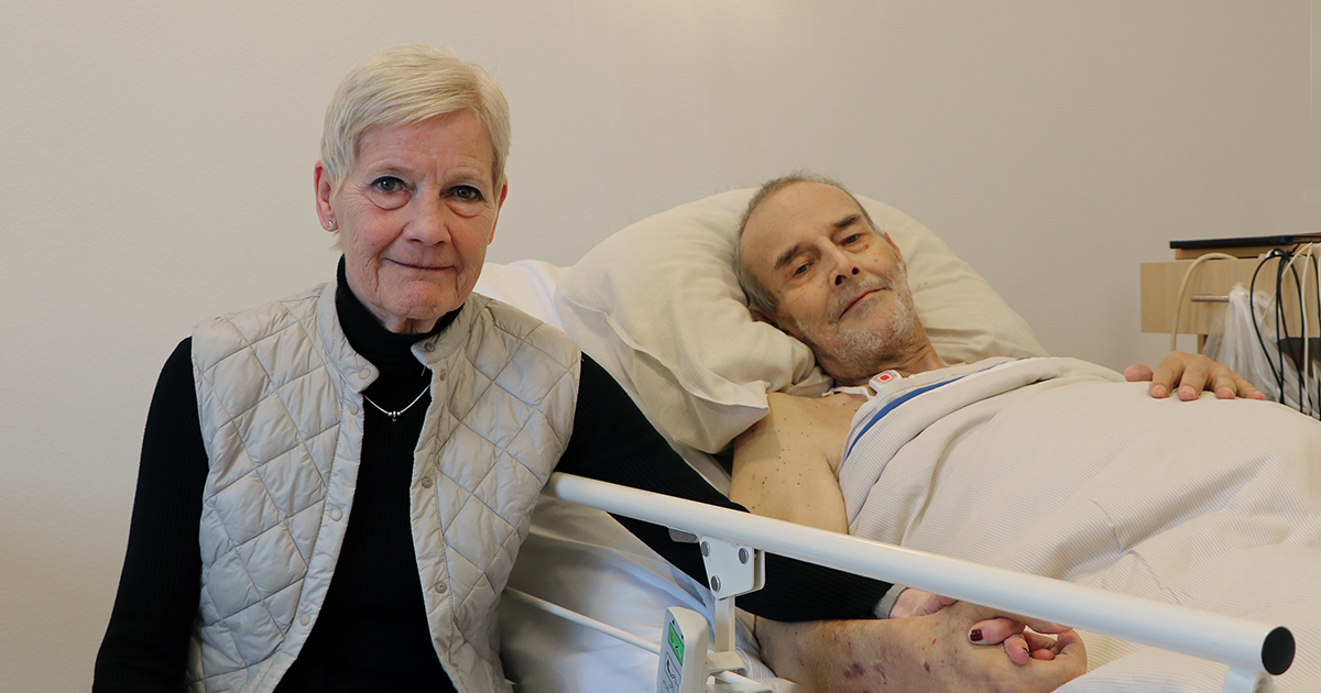 Billedet viser et ældre ægtepar ved en seng.