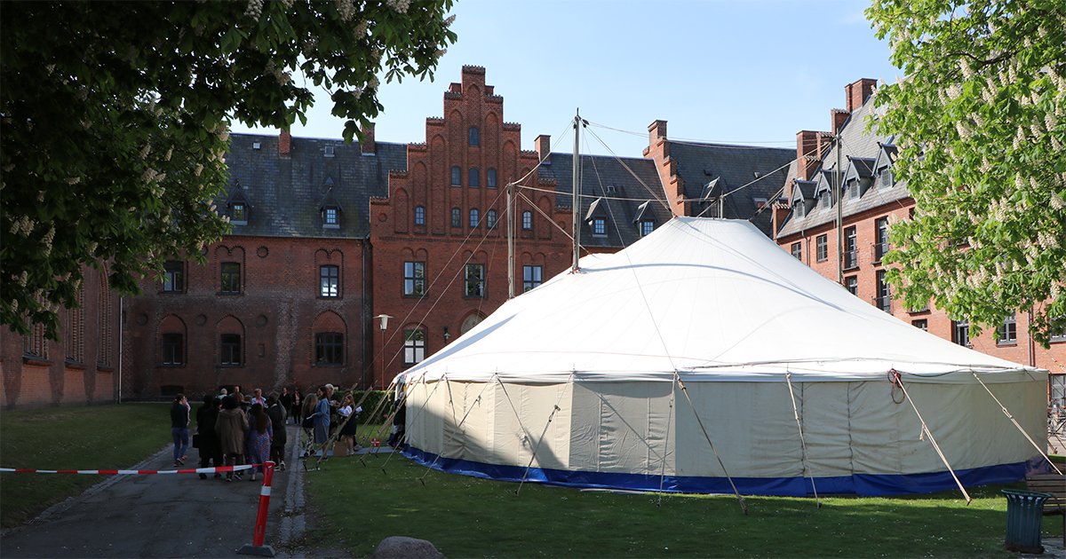 Billedet viser et telt foran en stor rød bygning.